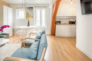A modern kitchen with white cabinets, a microwave, and a stove. There is a dining area with a white table and chairs, and a blue sofa.