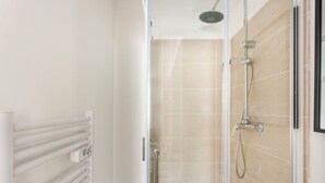 Une salle de bain moderne avec une douche à parois de verre, des carreaux de couleur beige et un radiateur blanc.