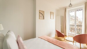 Une chambre avec un lit, deux chaises, un balcon avec vue et des œuvres d’art accrochées au mur.