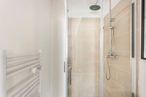 Une salle de bain moderne avec une douche à l’italienne en verre, des carreaux de couleur beige et un radiateur blanc.