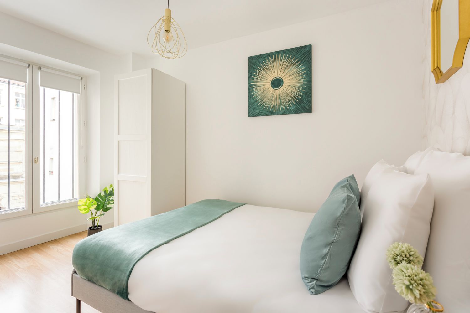 A bedroom with a bed, a green throw, a green pillow, a wall art piece, and a hanging light fixture.