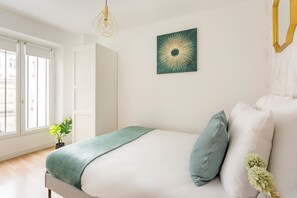 Une chambre à coucher avec un lit, un plaid vert, un coussin vert, une œuvre d’art murale et un luminaire suspendu.