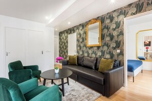 Una sala de estar moderna con un sofá de cuero oscuro, sillones verdes, una mesa redonda de centro y un papel tapiz floral.