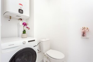 Un baño con lavadora, inodoro y una repisa con flores.