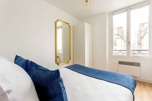 A bedroom with a bed, a large mirror, and a window with a view of buildings. - Merveil - Family Suite - Marais - Martin VI (Paris)