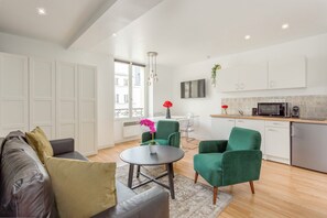A modern living room with a sofa, chairs, a coffee table, and a kitchen area with a microwave and cabinets. - Merveil - Family Suite - Marais - Martin VI (Paris)