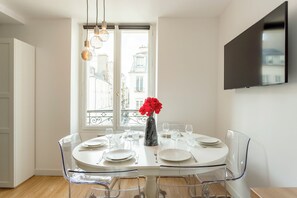 Un comedor con una mesa redonda dispuesta para cuatro personas, un florero con flores rojas y vistas a la ciudad a través de amplias ventanas.