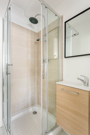 A modern bathroom with a glass shower enclosure, a wooden vanity, and a mirror. - Merveil - Family Suite - Marais - Martin VI (Paris)