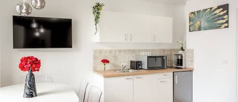 A modern kitchen with white cabinets, a microwave, a coffee maker, and a dining area with a round table and chairs.