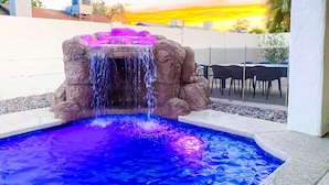 Una piscina con cascata a roccia e area relax con tavoli e sedie.