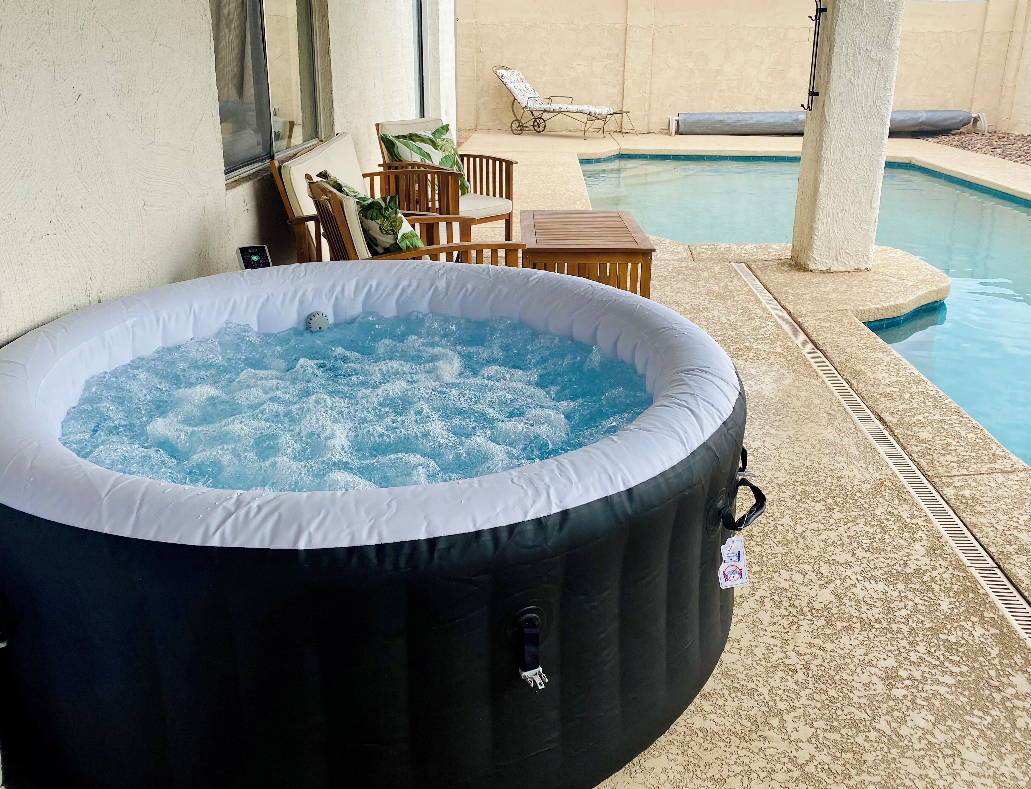 Een jacuzzi naast een zwembad met ligbedden en een tafel.