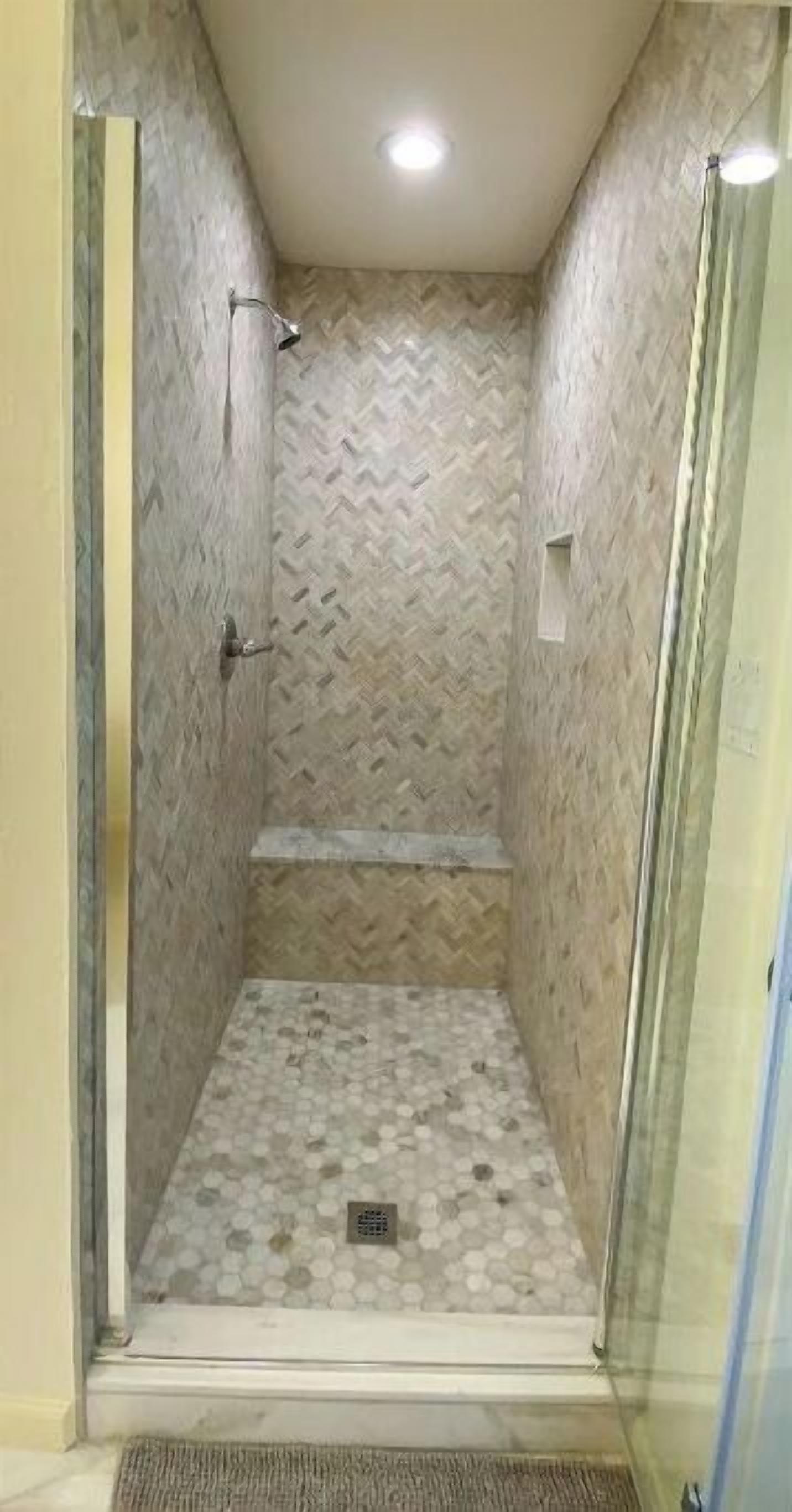 A small, enclosed shower area with a herringbone-patterned wall and a tiled floor.