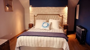 A bedroom with a large bed, a stone wall, and a radiator. - Domaine GILLE (Comblanchien)