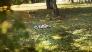A metal folding chair in a grassy area with trees in the background. - Domaine GILLE (Comblanchien)