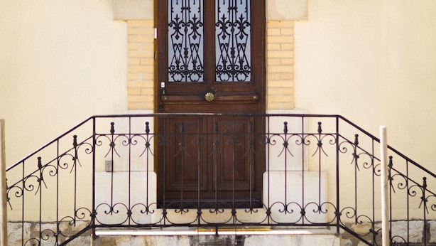 A building with a traditional architectural style, featuring a wooden door with decorative glass panels, a stone staircase, and a metal railing. - Domaine GILLE (Comblanchien)