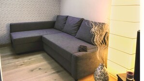 A corner room with a grey sofa, a small table, a vase with branches, and a skylight. - Domaine GILLE (Comblanchien)
