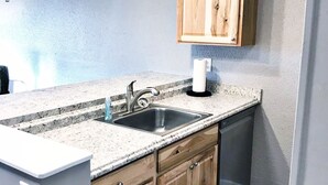Eine Küche mit einer Granitabdeckung, einer Edelstahlspüle, Holzschränken und einem Deckenventilator.