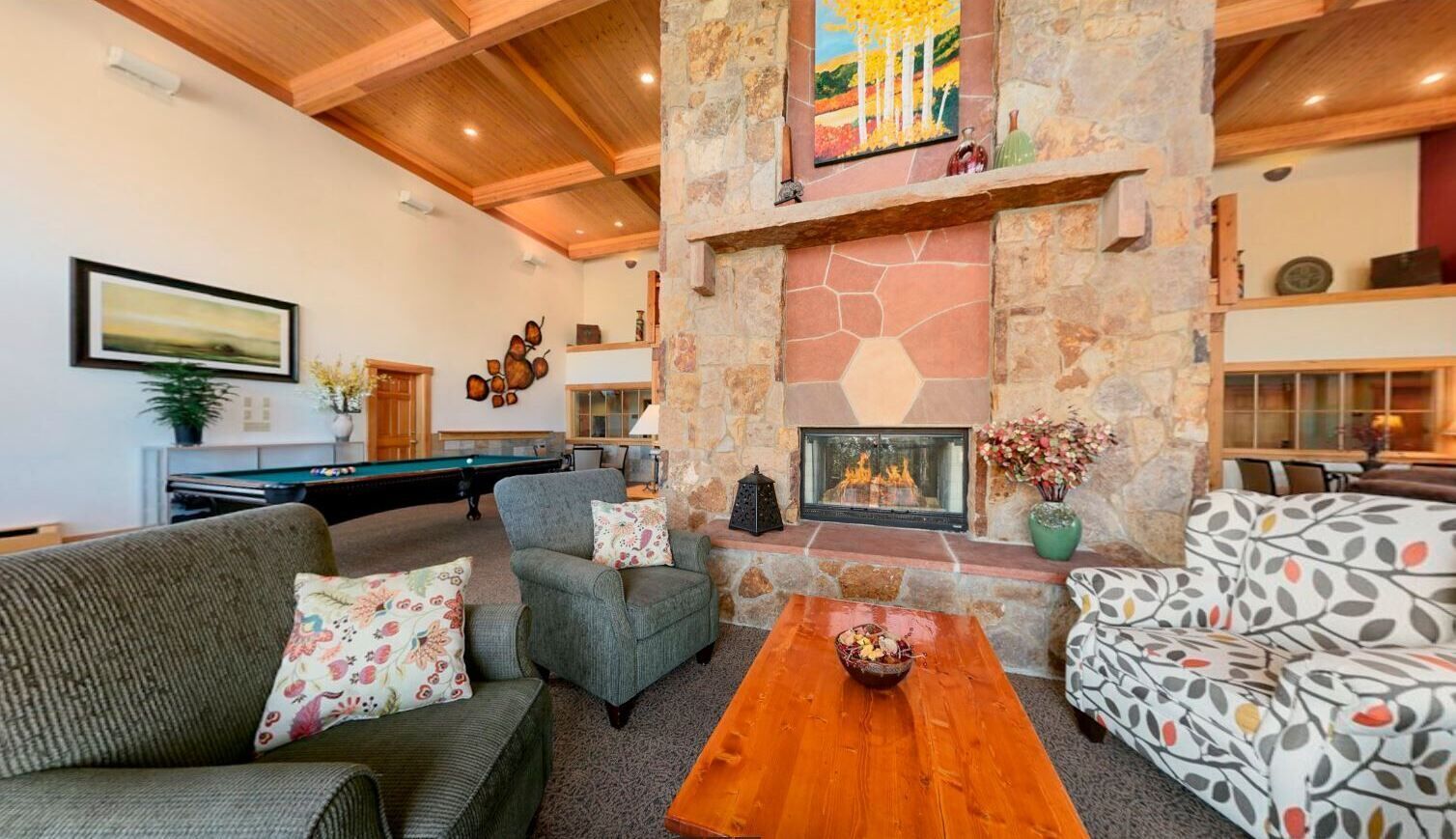 A cozy living room with a stone fireplace, comfortable seating, and a pool table.