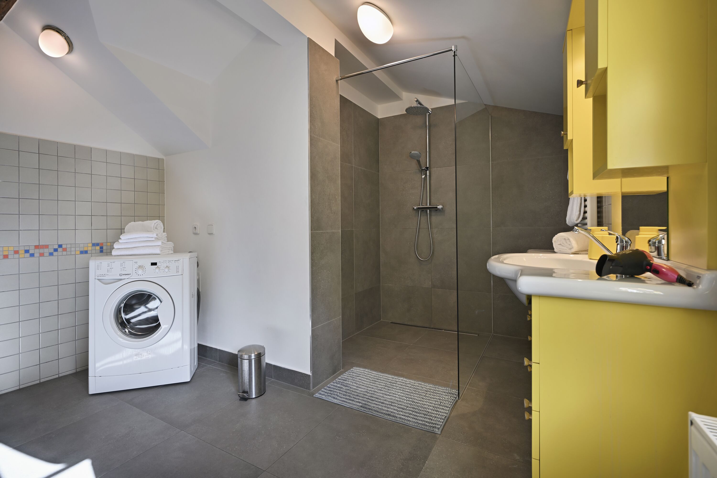Ein modernes Badezimmer mit Waschmaschine, einer Duschkabine und einem gelben Waschtisch.