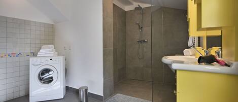 Ein modernes Badezimmer mit Waschmaschine, einer Duschkabine und einem gelben Waschtisch.