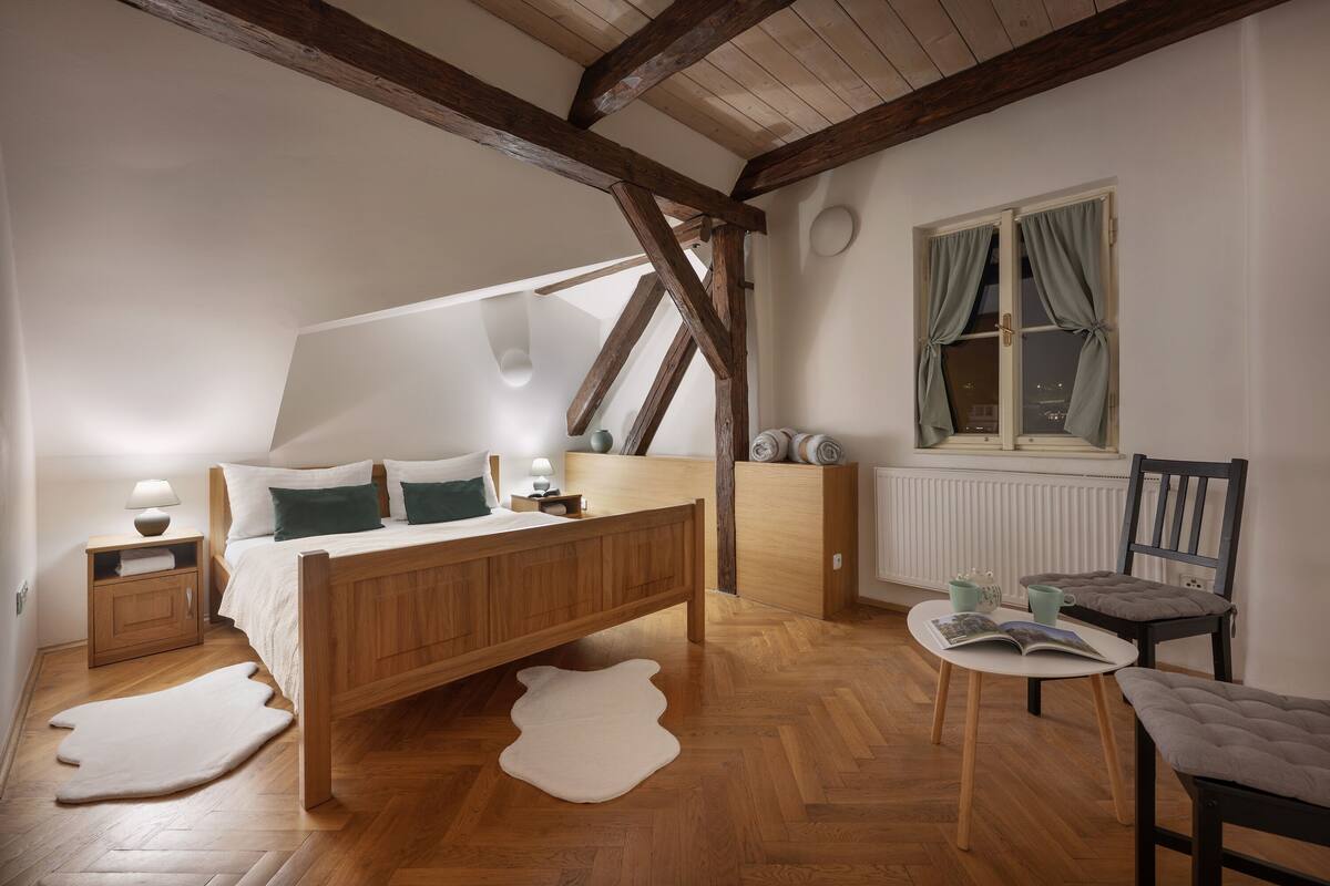Un dormitorio con una cama de madera, una mesita de noche, un sillón para leer y una ventana con cortinas.