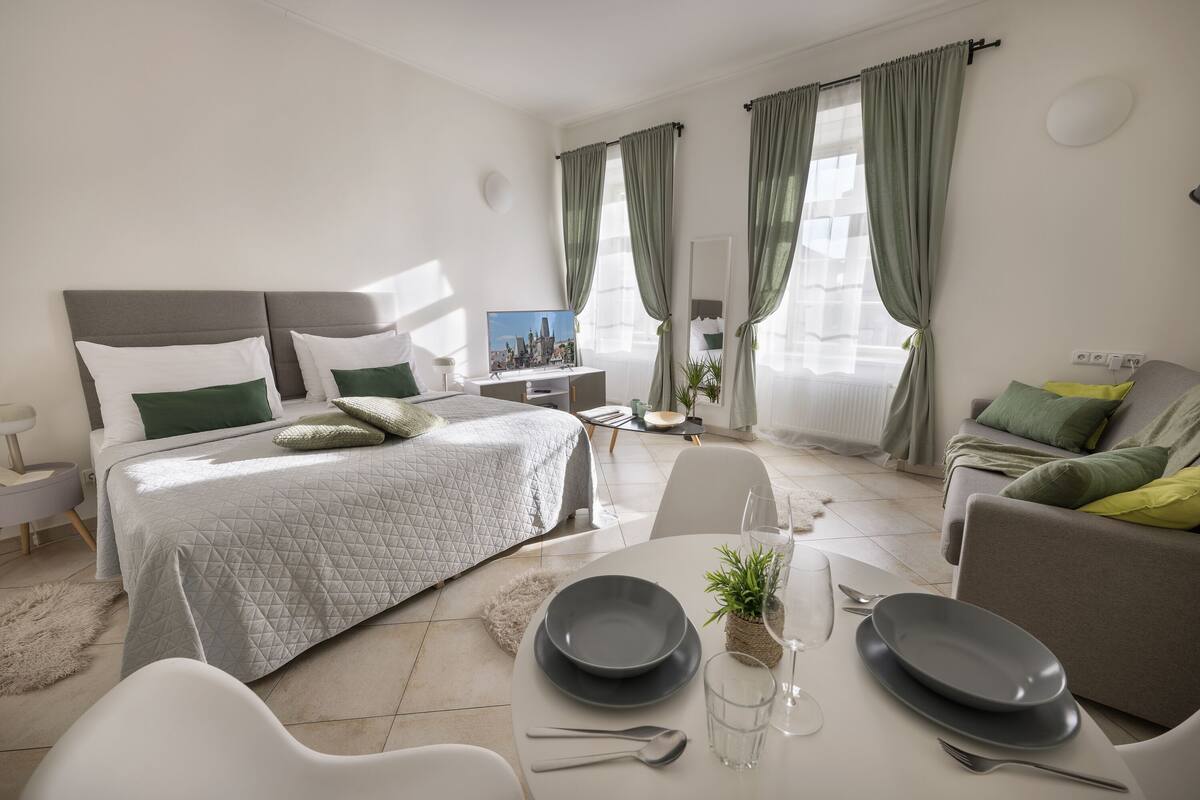 Una habitación de hotel moderna con una cama, una mesa de comedor con platos, vasos y cubiertos, y un sofá con cojines.