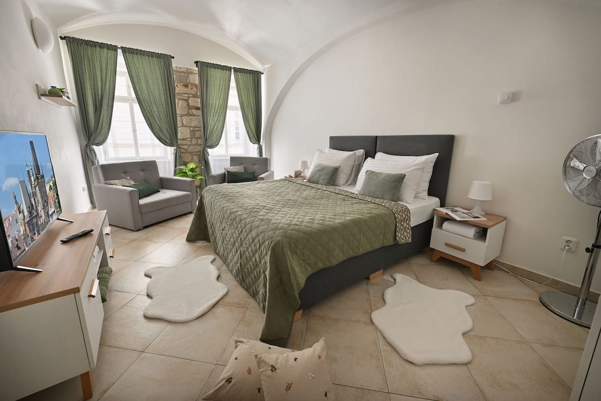 Un dormitorio con una cama, un escritorio, una silla, una mesita de noche, una lámpara y un ventilador.