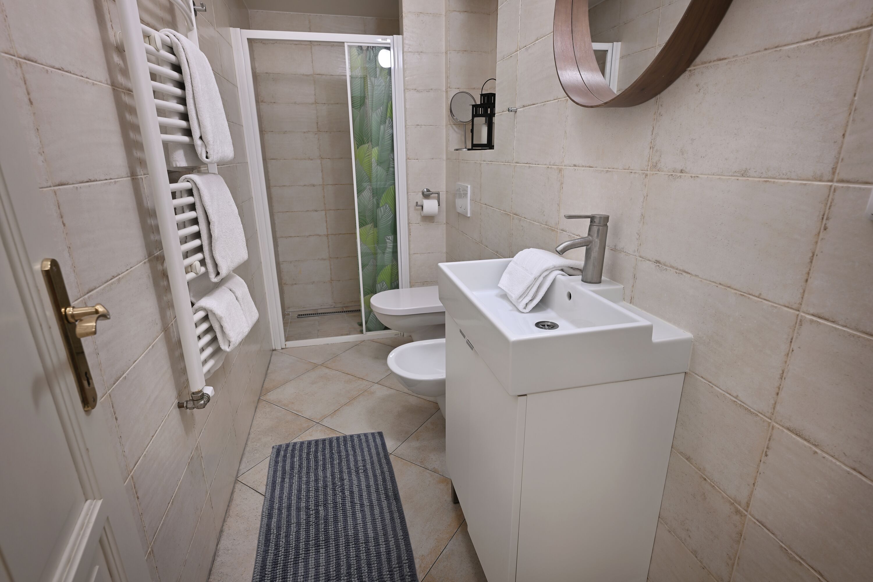 Un bagno con lavandino bianco, servizi igienici e zona doccia. Presente un portasciugamani con diversi asciugamani, un piccolo specchio e un asciugamano sul lavandino.