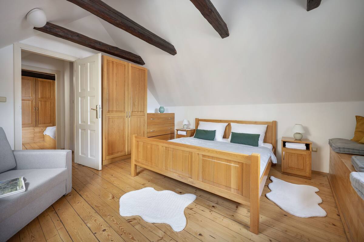 Un dormitorio con una cama de madera, un sofá gris, suelo de madera y un tapete de cuero de vaca blanco.