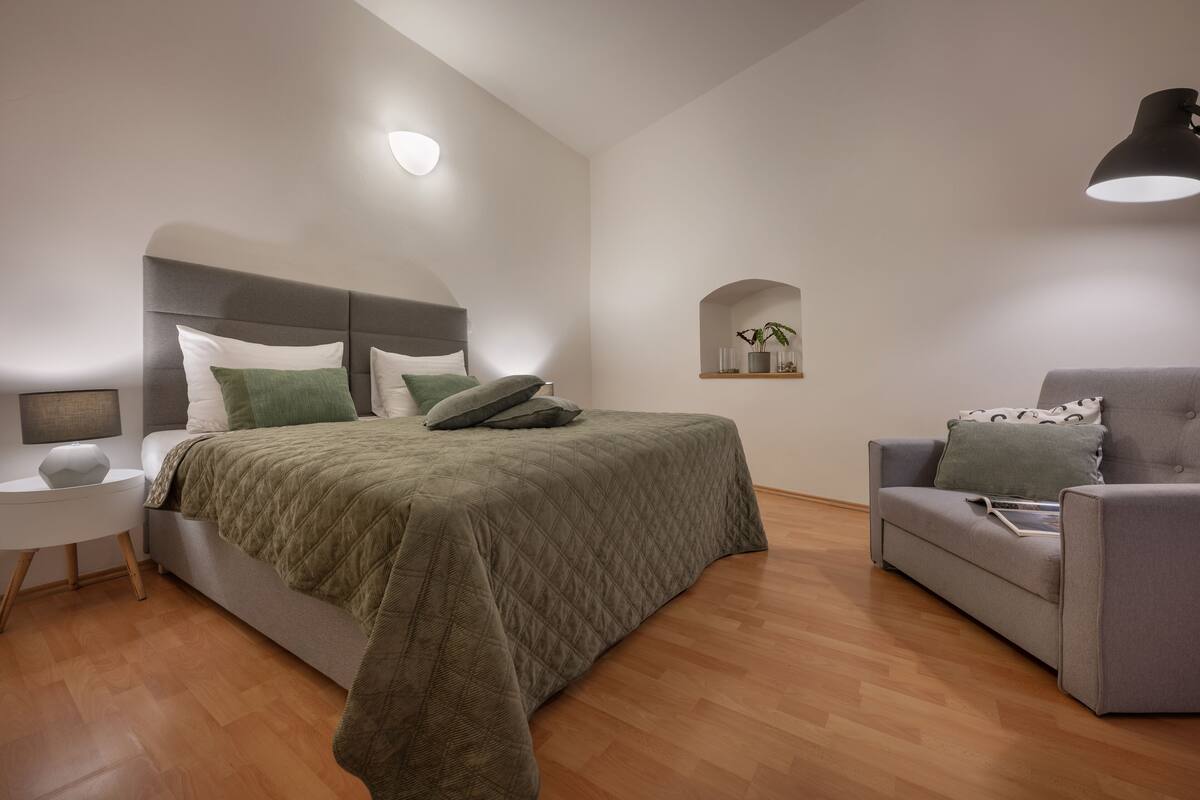 Un dormitorio moderno con una cama, una mesita de noche, una silla y una estantería con una planta.