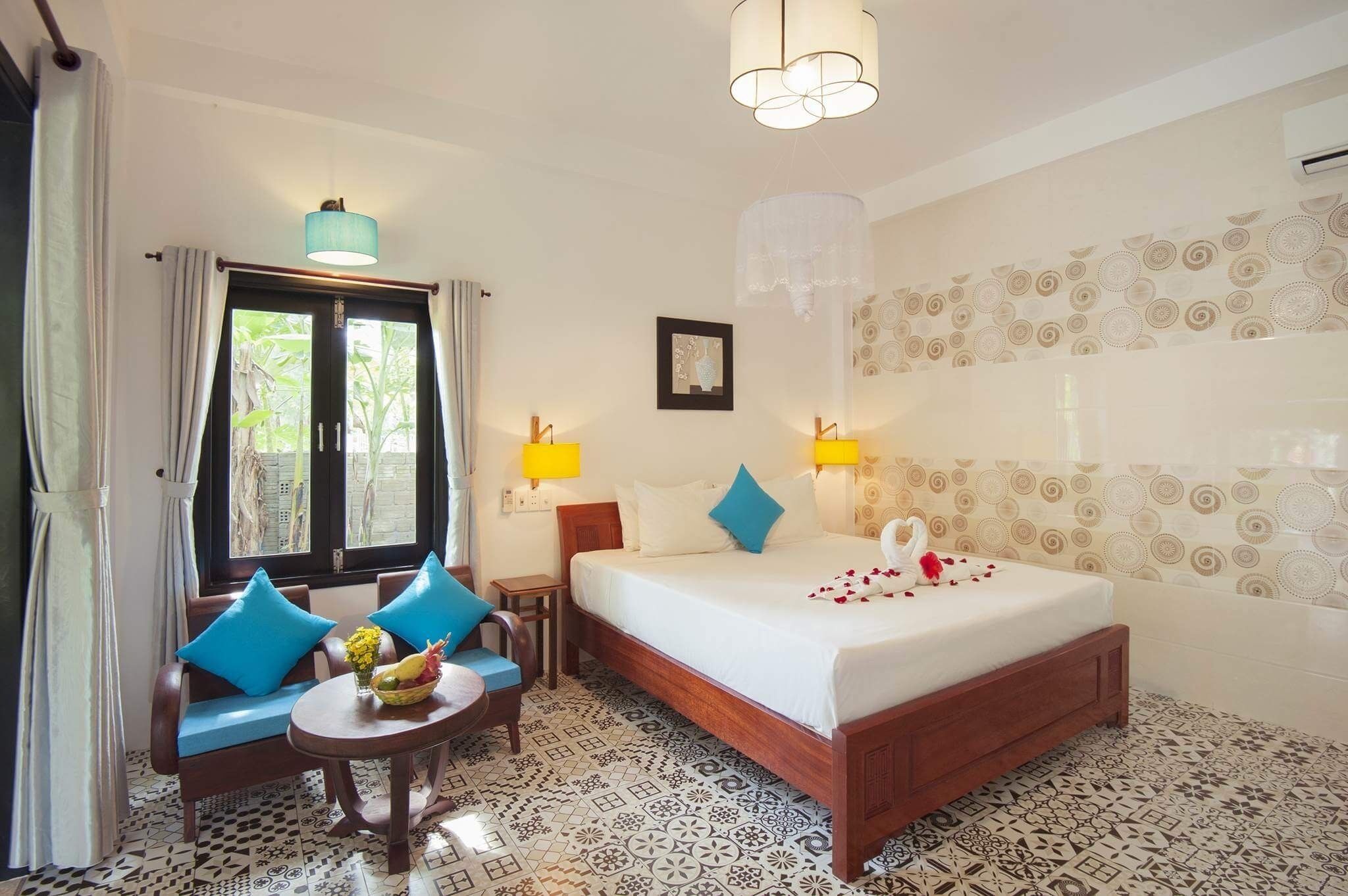 A hotel room with a bed, two chairs, a small table with a vase, and a window with curtains.