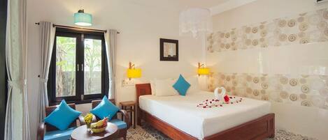 A hotel room with a bed, two chairs, a small table with a vase, and a window with curtains.