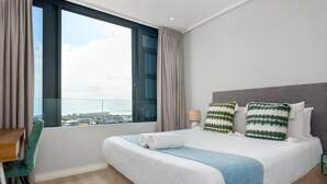 Et hotelværelse med en stor seng, et skrivebord og udsigt over byen gennem et stort vindue.