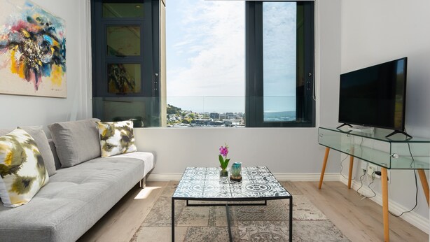 En moderne stue med en grå sofa, et glasbord og et fjernsyn på et glasmøbel.