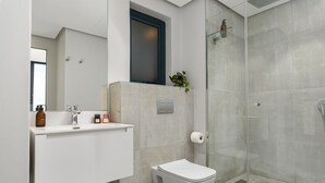 Et moderne badeværelse med hvid kommode, toilet og brusekabine med glasvægge.