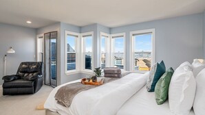 Un dormitorio con una cama grande, una silla, un ventanal con vistas y una lámpara de pie.