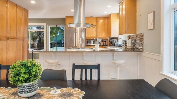 Una cocina moderna con armarios de madera, campana extractora de acero inoxidable y una isla central con taburetes de bar.