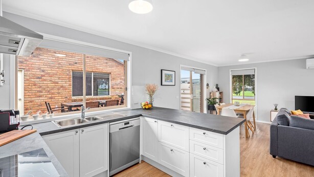A modern kitchen with white cabinetry, a built-in oven, and a large window overlooking a brick wall. - Parrwang Rest - Renovated cosy unit in a Serene Location. (Portarlington)