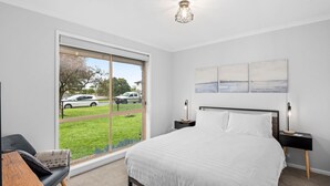 A modern bedroom with a large window, a bed, two bedside tables, and a wall-mounted artwork. - Parrwang Rest - Renovated cosy unit in a Serene Location. (Portarlington)