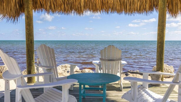 A wooden deck with white Adirondack chairs and a turquoise table, overlooking a calm sea. - Overlooking the Lagoon and Pool (Key Largo)