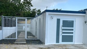 A small, single-story building with a white exterior and a blue roof. It features a set of white metal gates and a small staircase leading to a door. - Ocean Side PR (Carolina)
