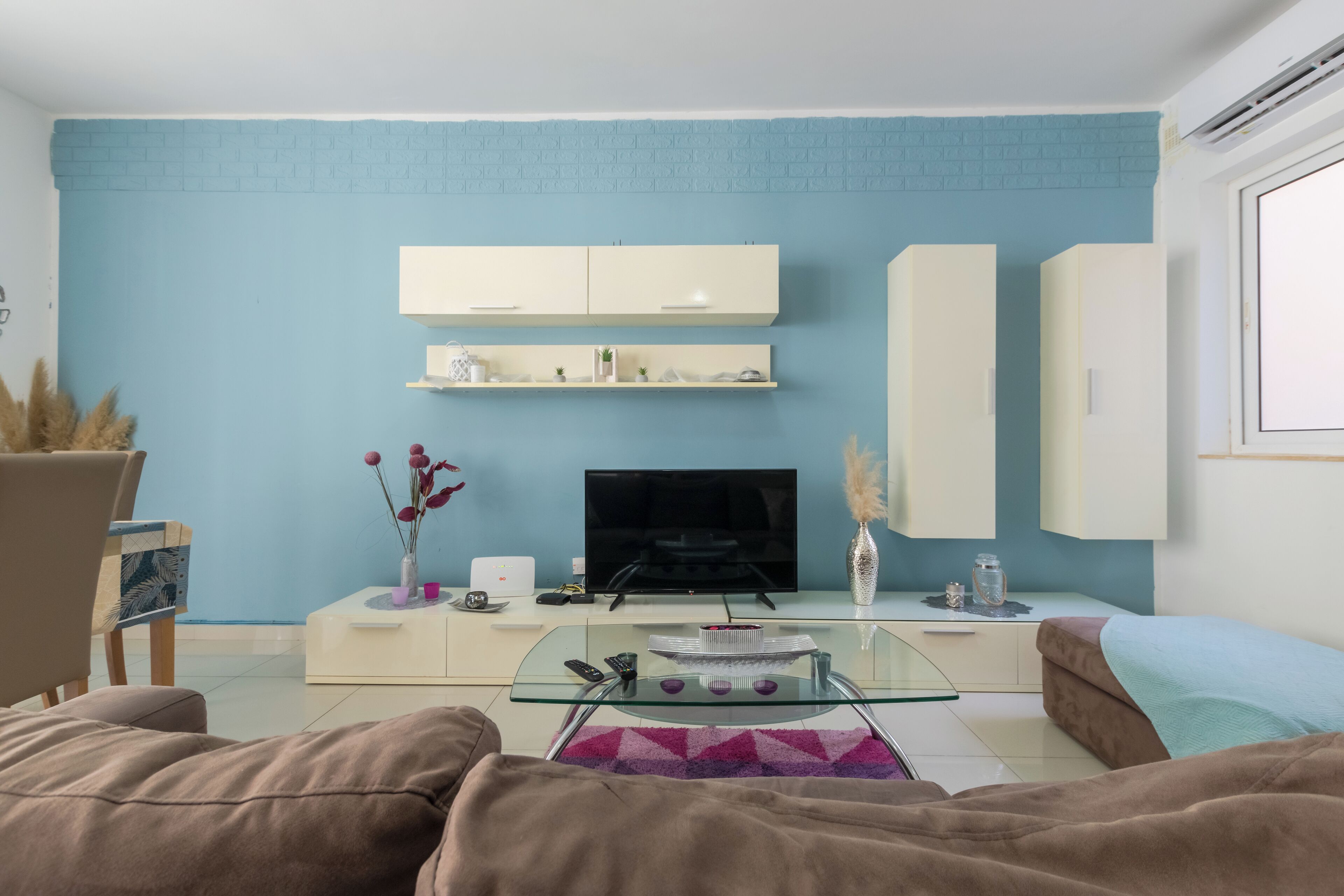 Un salon avec un mur en briques bleues, un téléviseur à écran plat, une table basse en verre et un canapé.