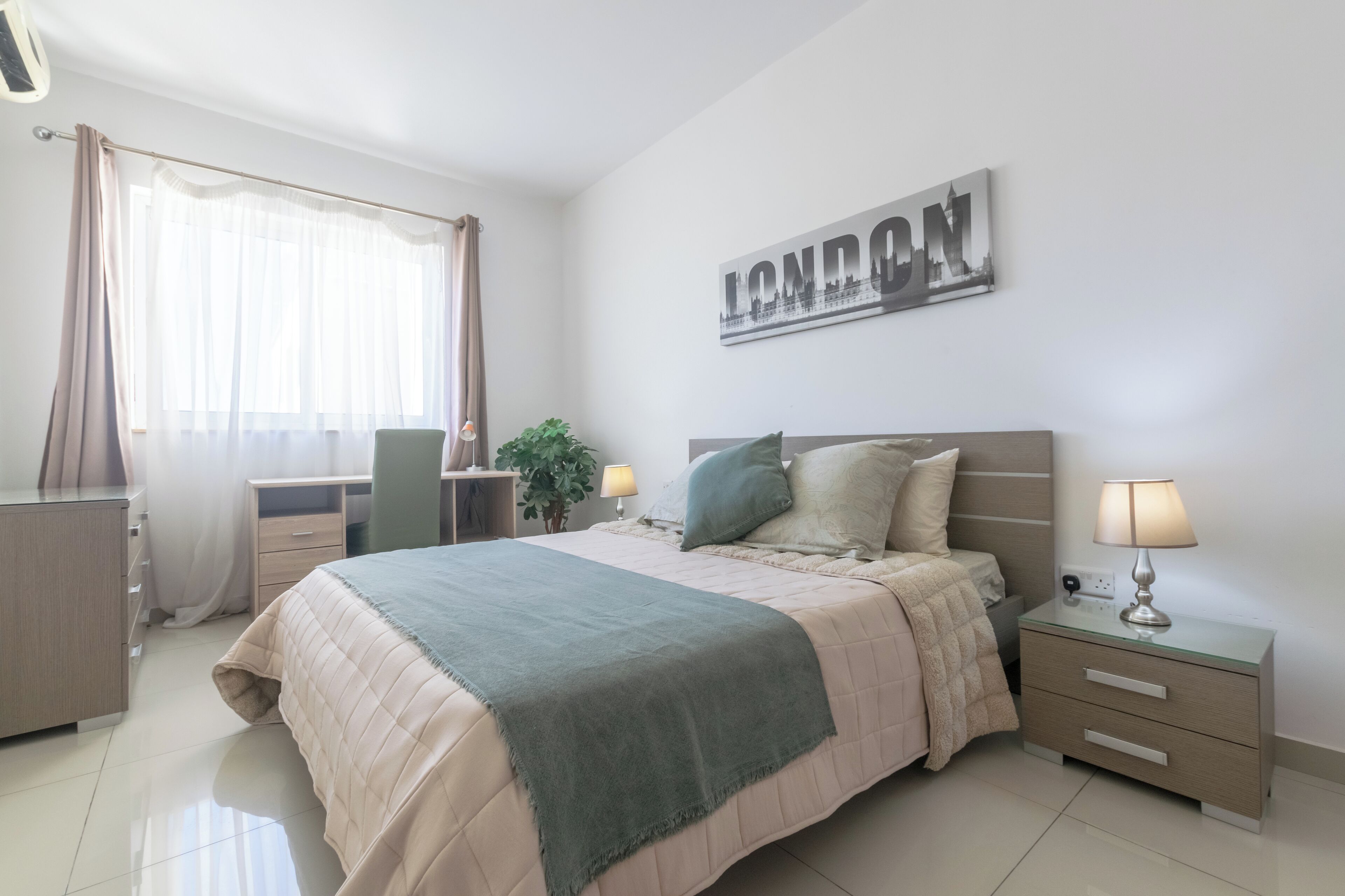 A bedroom with a bed, bedside tables, a desk, and a wall-mounted sign.