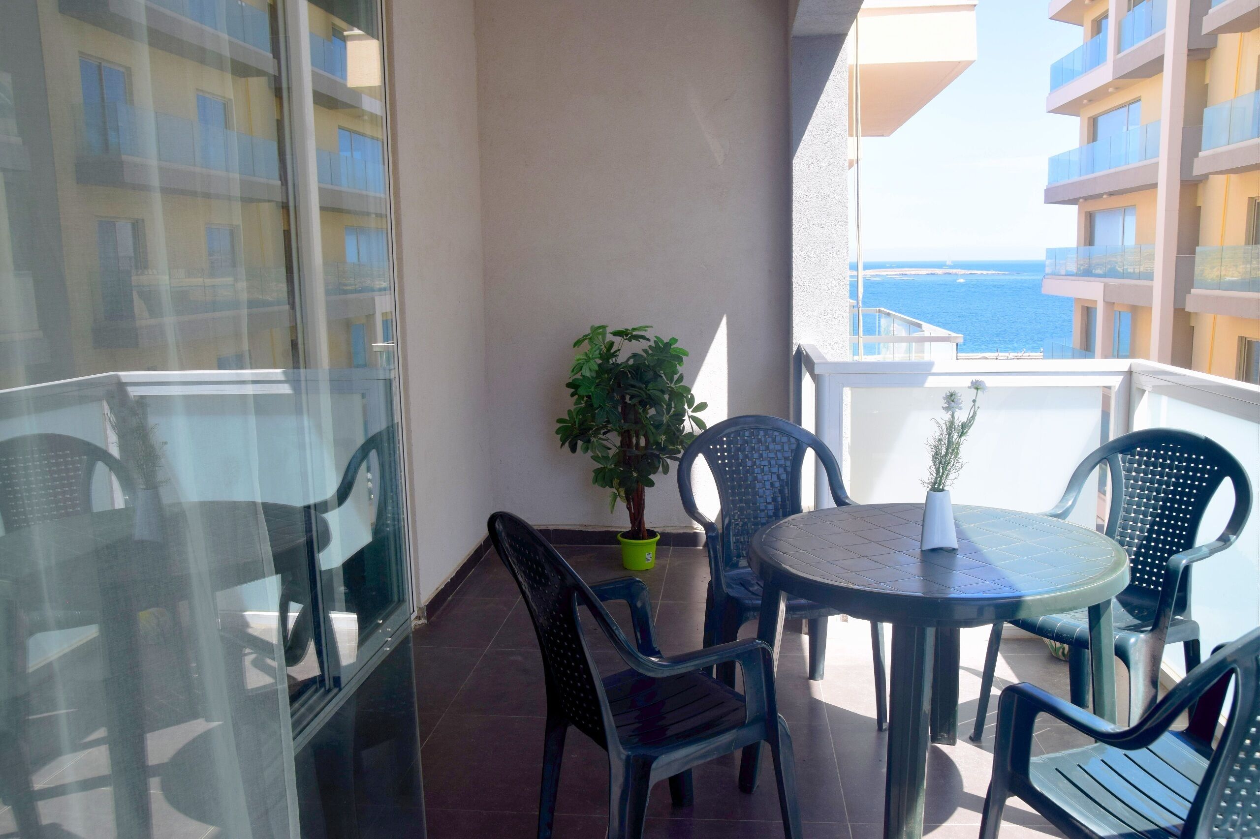 A balcony with a table and chairs, a potted plant, and a view of the sea.
