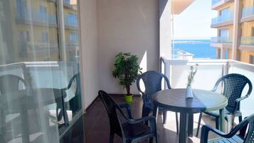 A balcony with a table and chairs, a potted plant, and a view of the sea.