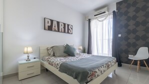 A bedroom with a bed, a nightstand with a lamp, a chair, and a wall with a 'PARIS' sign. - ☆☆Amazing Apartment w/side sea view☆☆ 1 (St. Pauls Bay, Malta)