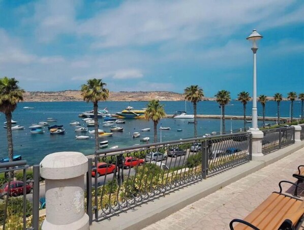 Un paseo marítimo con vistas al mar, coches aparcados y una hilera de palmeras.