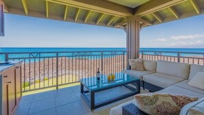 Un balcone con un tavolino in vetro, una divanetto bianco e vista sulla spiaggia e sull'oceano.