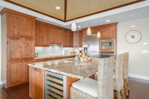 A modern kitchen with wooden cabinets, a granite countertop, stainless steel appliances, and wicker chairs.