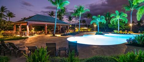 A pool area with lounge chairs, a covered seating area, and palm trees.